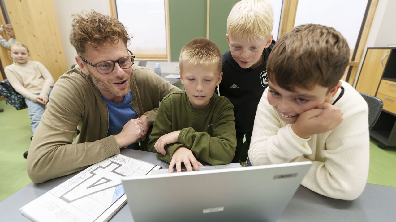 Børn i indskolingen kigger på pc sammen med voksen