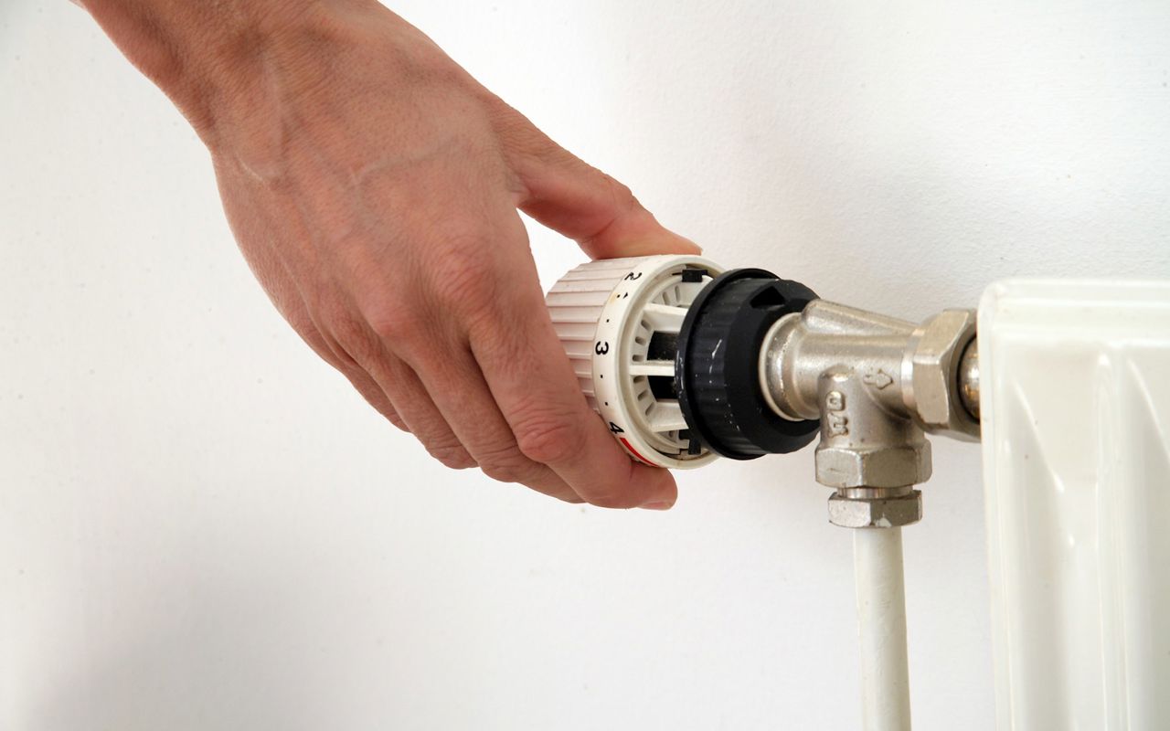 En hånd drejer på en termostat på en radiator