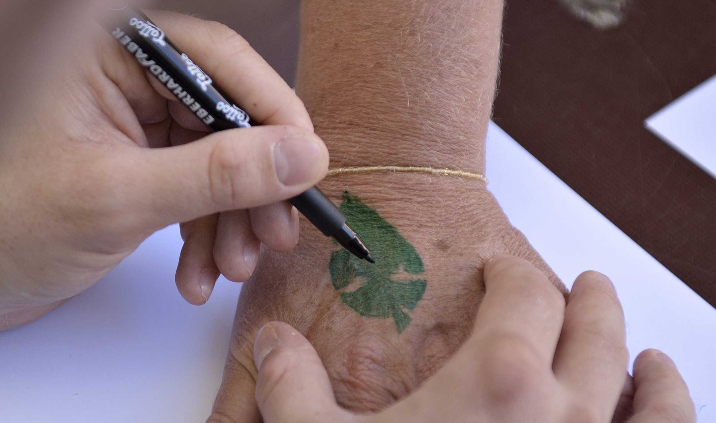 En hånd med en tusch tegner logo for Grønne Sammen på en anden persons håndryg