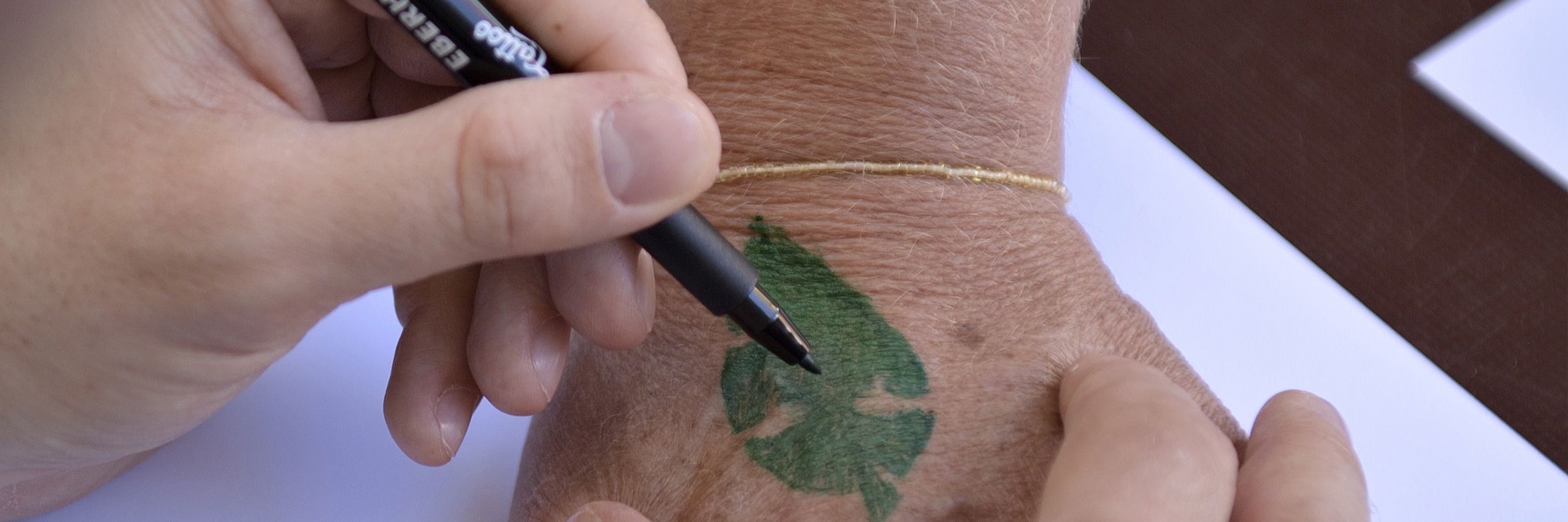 En hånd med en tusch tegner logo for Grønne Sammen på en anden persons håndryg